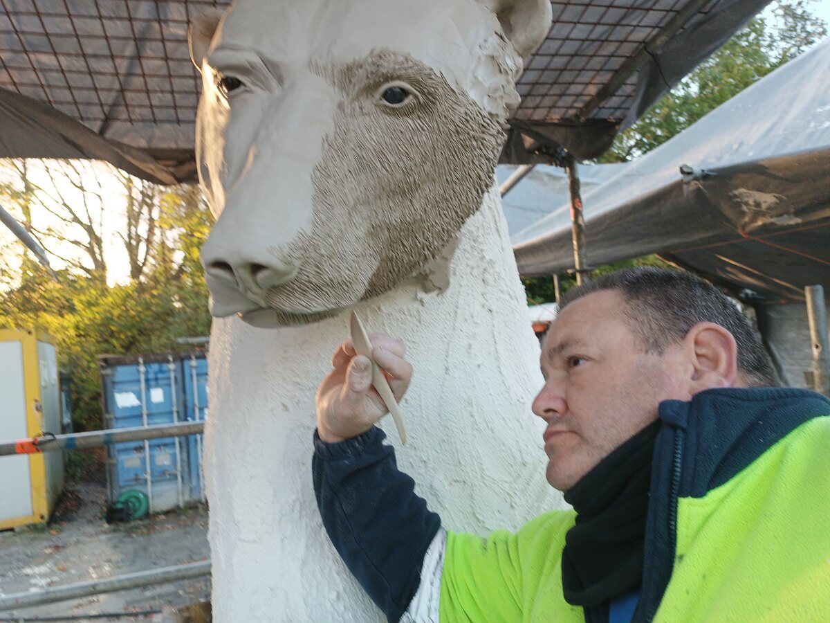 Sculptor beside a large modelled head during the making process